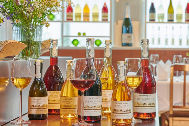 Many bottles of Delmosa non-alcoholic beverage bottles on display in a restaurant with wine glasses and a well lit background.